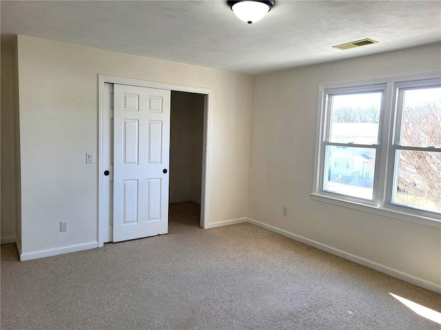 carpeted empty room with baseboards, visible vents, and a textured ceiling