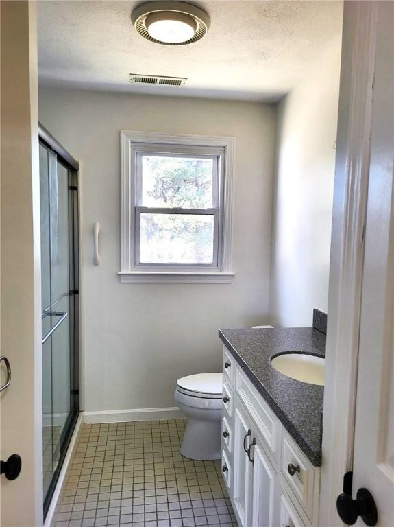 bathroom featuring a textured ceiling, toilet, vanity, visible vents, and a shower stall