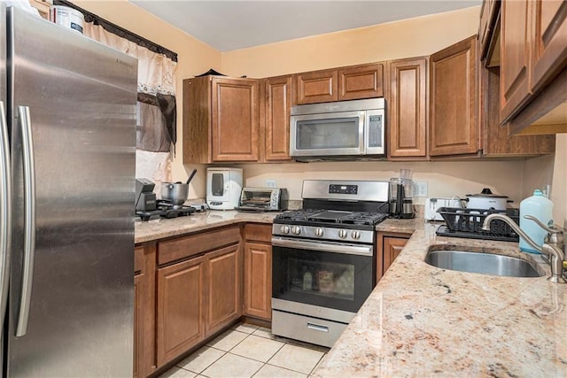 kitchen with stainless steel appliances, light stone counters, brown cabinetry, and a sink