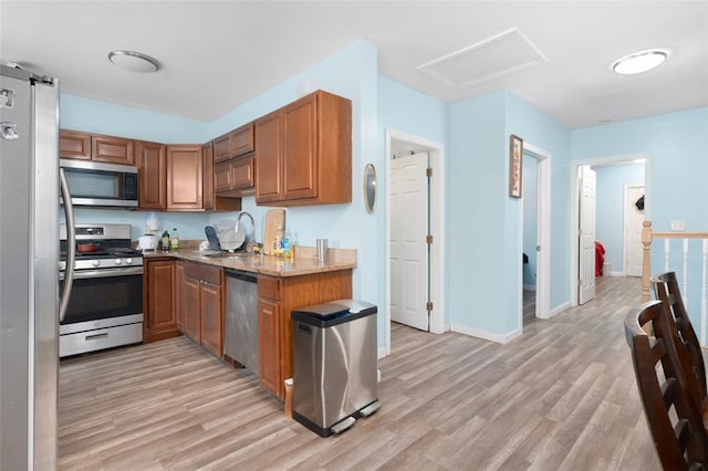 kitchen with stainless steel appliances, light wood finished floors, brown cabinetry, and a sink