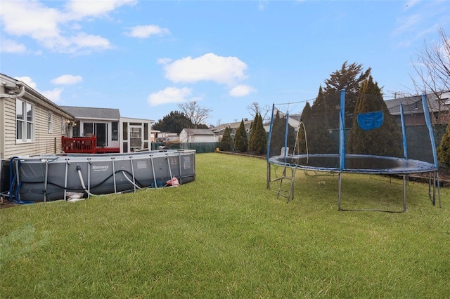 view of yard featuring a trampoline, an empty pool, and fence