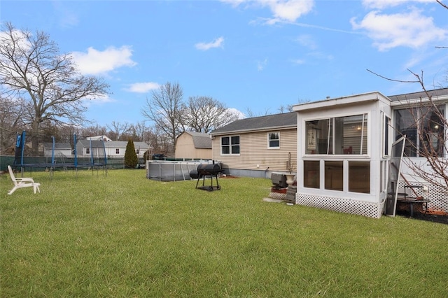 rear view of property with a lawn, a trampoline, a sunroom, and an outdoor pool