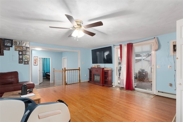 living area featuring a baseboard heating unit, wood finished floors, and a ceiling fan