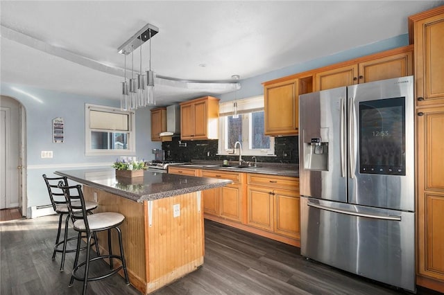 kitchen featuring arched walkways, appliances with stainless steel finishes, decorative light fixtures, a center island, and wall chimney range hood