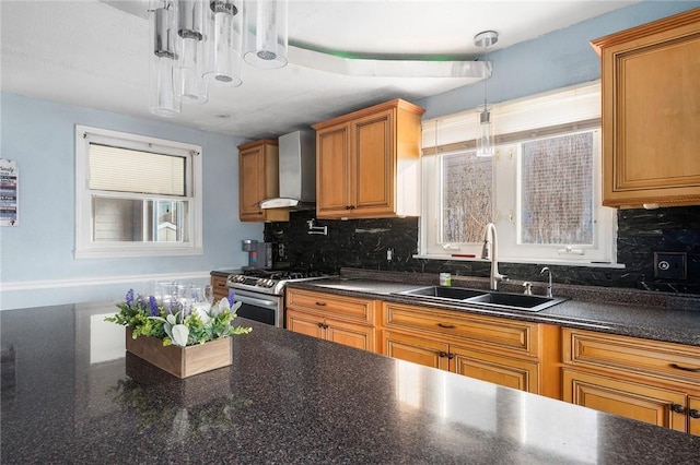 kitchen with dark countertops, hanging light fixtures, wall chimney range hood, and gas range