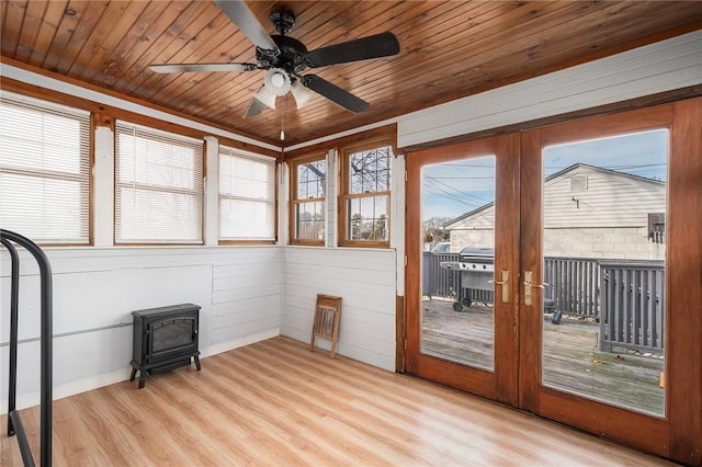 unfurnished sunroom with a wood stove, wooden ceiling, and ceiling fan