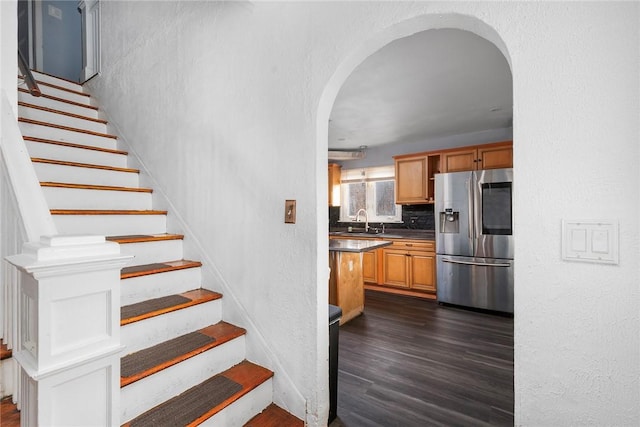 stairs with arched walkways, wood finished floors, and a textured wall