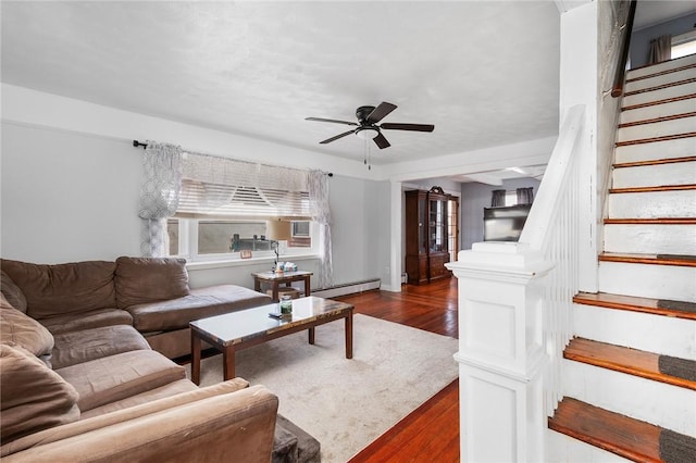 living area with a ceiling fan, stairway, baseboard heating, and dark wood-style flooring