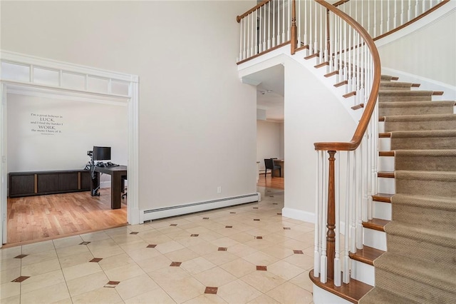 foyer with stairway, a high ceiling, a baseboard heating unit, tile patterned flooring, and baseboards