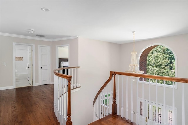 corridor with dark wood finished floors, a notable chandelier, visible vents, ornamental molding, and an upstairs landing