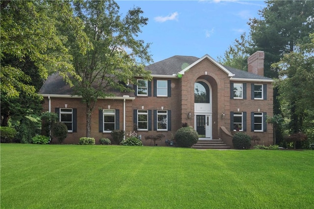 colonial home with a chimney, a front lawn, and brick siding