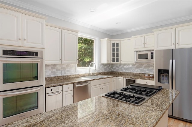 kitchen with light stone counters, stainless steel appliances, a sink, ornamental molding, and glass insert cabinets