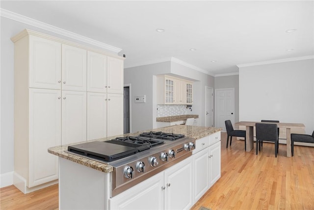 kitchen featuring light wood finished floors, a kitchen island, glass insert cabinets, and white cabinetry