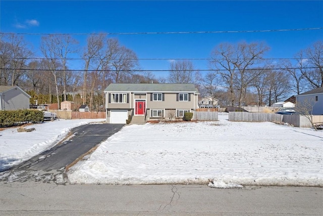 raised ranch with an attached garage, fence, and aphalt driveway