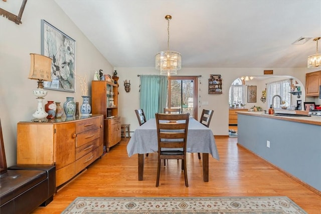 dining space featuring arched walkways, vaulted ceiling, a notable chandelier, and light wood finished floors