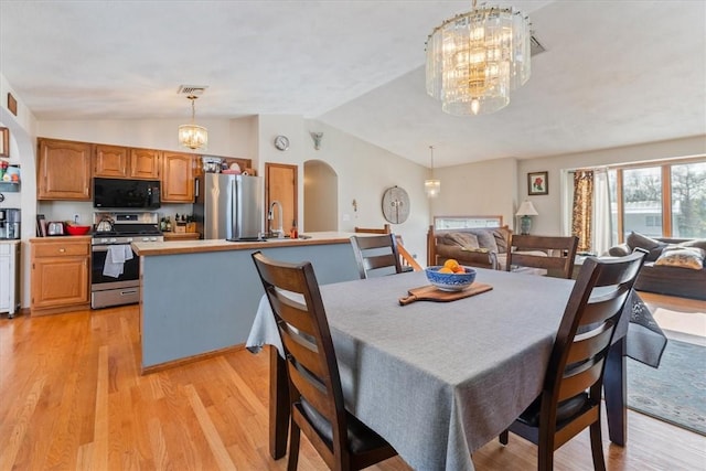 dining room with arched walkways, light wood finished floors, lofted ceiling, and an inviting chandelier