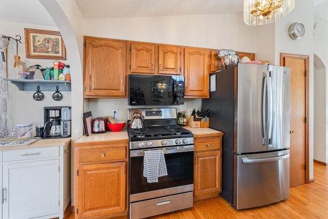 kitchen featuring stainless steel appliances, brown cabinets, light countertops, and light wood-style floors