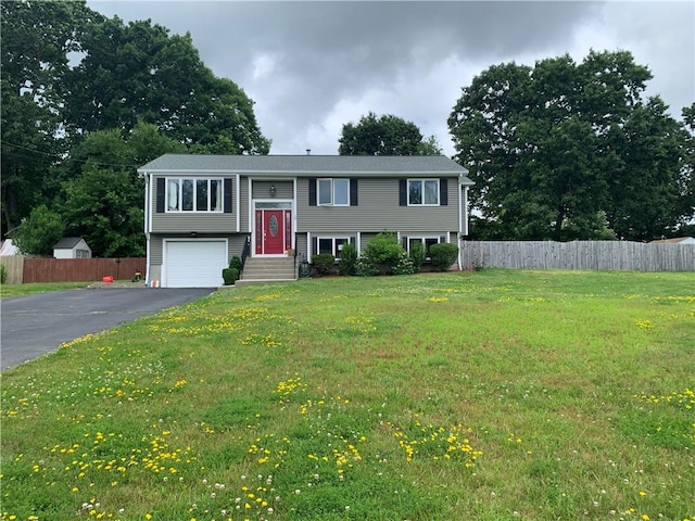 raised ranch featuring fence, driveway, and a front lawn