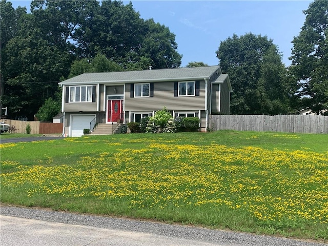 raised ranch with a front lawn, fence, driveway, and an attached garage