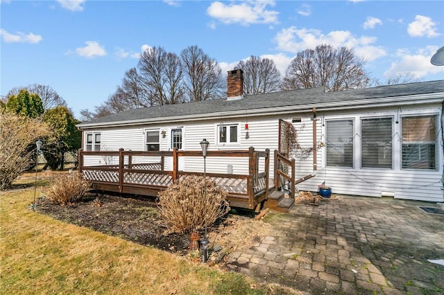 back of house featuring a patio area, a chimney, a deck, and a lawn