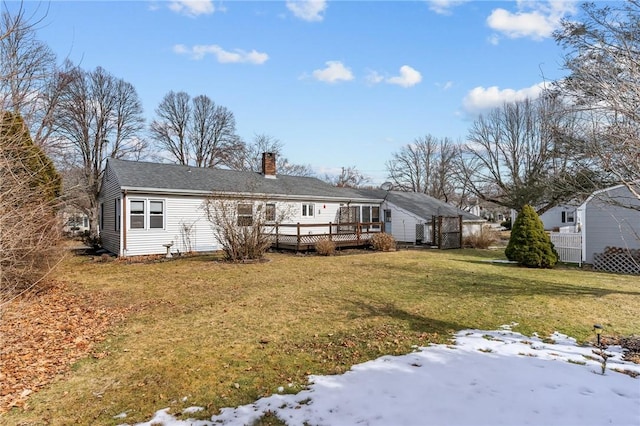 snow covered house with a deck, a lawn, and a chimney