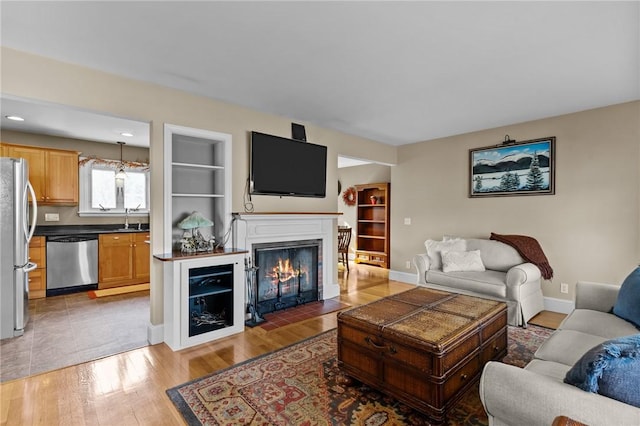 living area with a fireplace with flush hearth, wood-type flooring, baseboards, and built in features