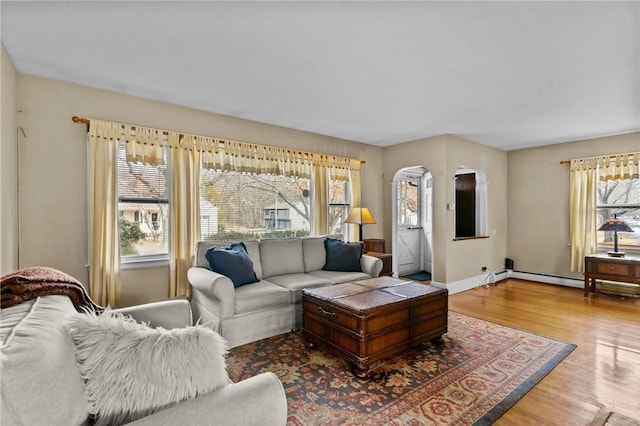 living area with arched walkways, baseboard heating, wood finished floors, and baseboards