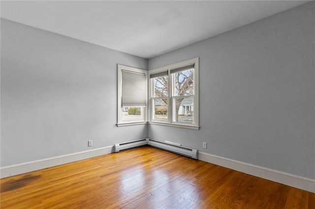 unfurnished room featuring baseboards, a baseboard heating unit, and wood finished floors