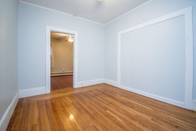 empty room featuring a baseboard radiator, crown molding, baseboards, and wood finished floors