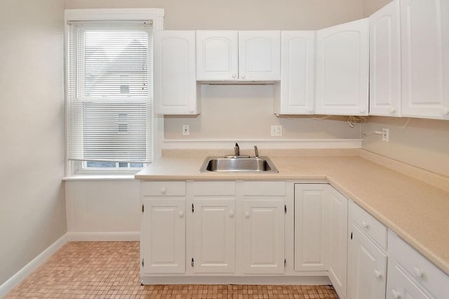 kitchen featuring white cabinets, light countertops, a sink, and baseboards