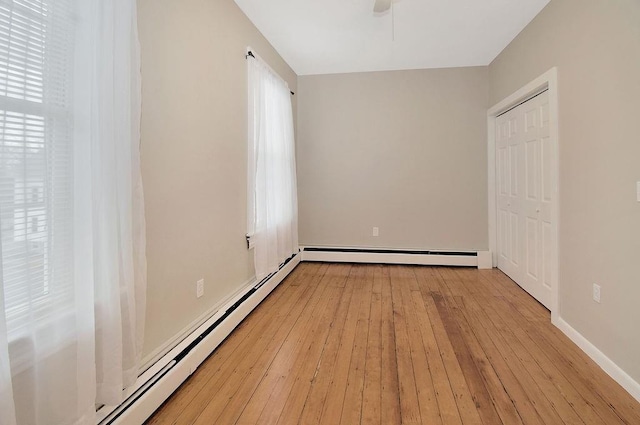 empty room with a ceiling fan, baseboard heating, light wood-style flooring, and baseboards