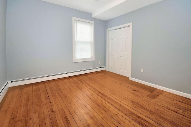 unfurnished bedroom with a baseboard heating unit, a closet, light wood-style floors, and baseboards