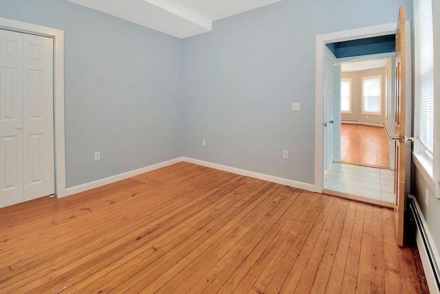 unfurnished bedroom featuring light wood finished floors, baseboards, baseboard heating, and a closet