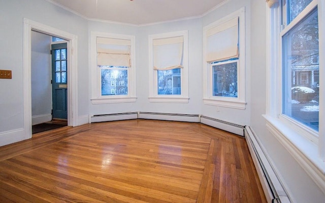 empty room featuring ornamental molding, baseboard heating, wood finished floors, and baseboards