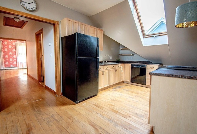 kitchen with dark countertops, lofted ceiling with skylight, a sink, light wood-type flooring, and black appliances