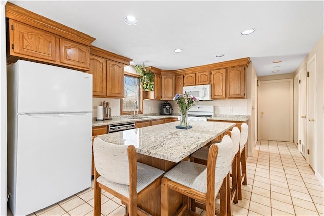 kitchen with a sink, white appliances, light stone counters, and light tile patterned flooring