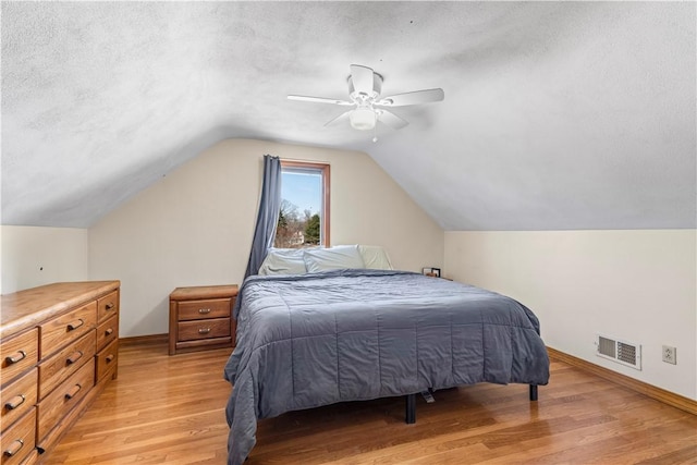 bedroom featuring baseboards, visible vents, light wood-style flooring, vaulted ceiling, and a textured ceiling