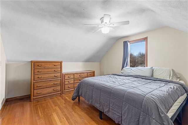 bedroom featuring light wood finished floors, baseboards, ceiling fan, lofted ceiling, and a textured ceiling