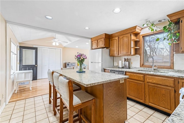 kitchen featuring a center island, a breakfast bar, lofted ceiling, freestanding refrigerator, and a sink