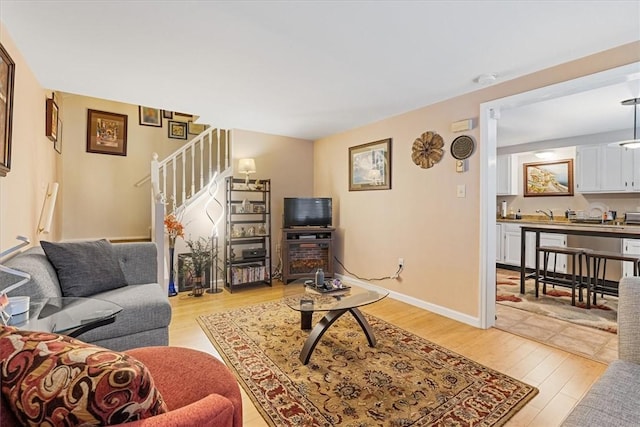 living area featuring light wood-style floors, stairway, and baseboards