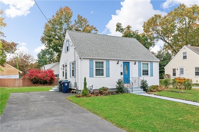 view of front of home with aphalt driveway, roof with shingles, a front yard, and fence