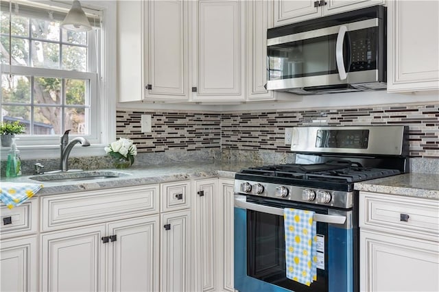 kitchen featuring appliances with stainless steel finishes, white cabinetry, a sink, and backsplash