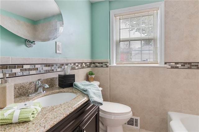 bathroom featuring a tub to relax in, visible vents, toilet, vanity, and tile walls