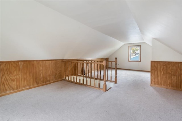 bonus room with lofted ceiling, wood walls, wainscoting, and light colored carpet