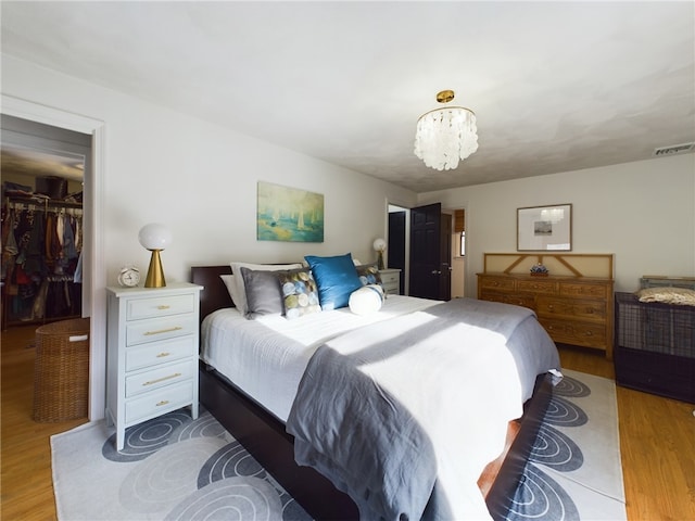 bedroom with light wood finished floors, visible vents, a walk in closet, a chandelier, and a closet