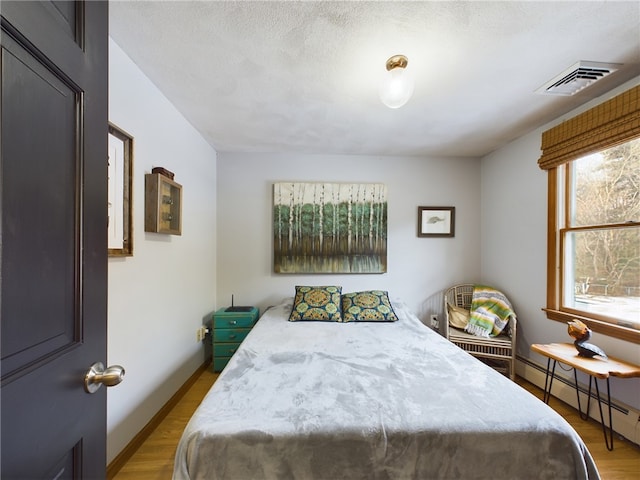 bedroom with baseboards, visible vents, light wood-style flooring, and baseboard heating