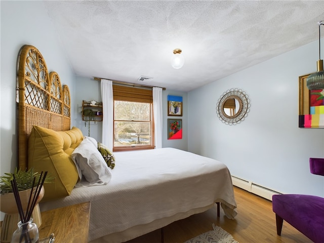 bedroom with visible vents, a textured ceiling, a baseboard heating unit, and wood finished floors