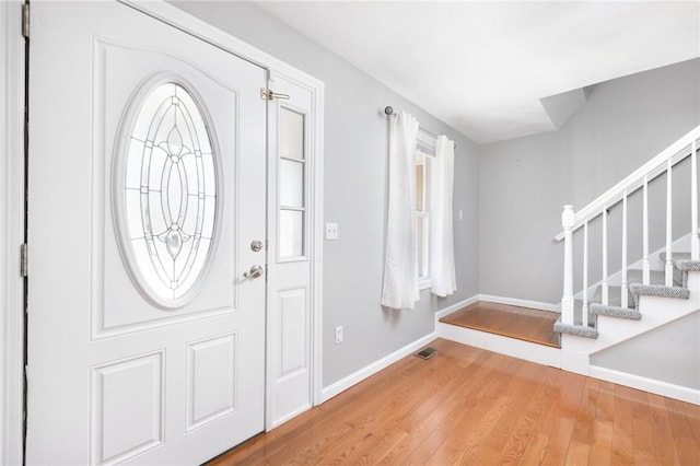 foyer with baseboards, visible vents, stairway, and wood finished floors