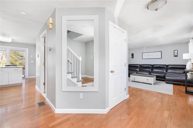 hall with visible vents, light wood-style flooring, baseboards, and stairs