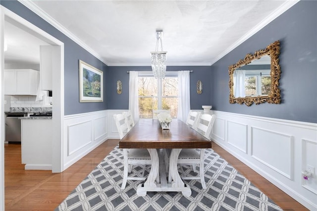 dining area featuring a notable chandelier, ornamental molding, wood finished floors, and wainscoting